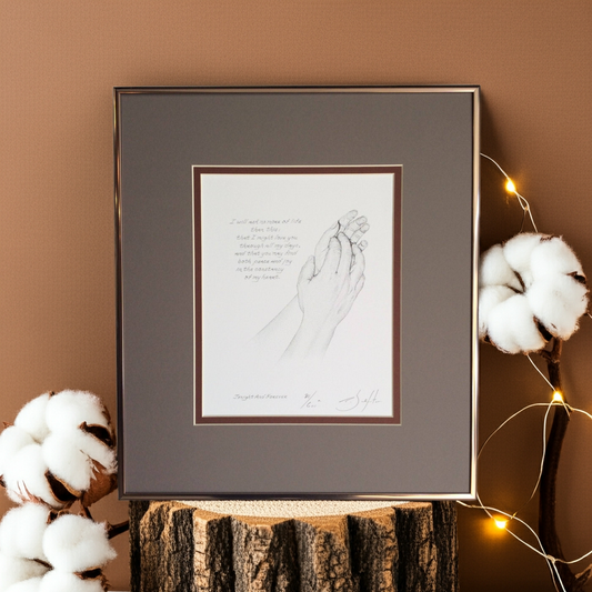 Framed artwork of hands on a wooden surface with cotton and string lights in the background