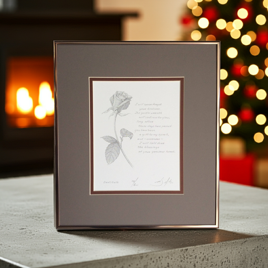 Framed artwork with a rose illustration and poem on a surface with a blurred festive background.
