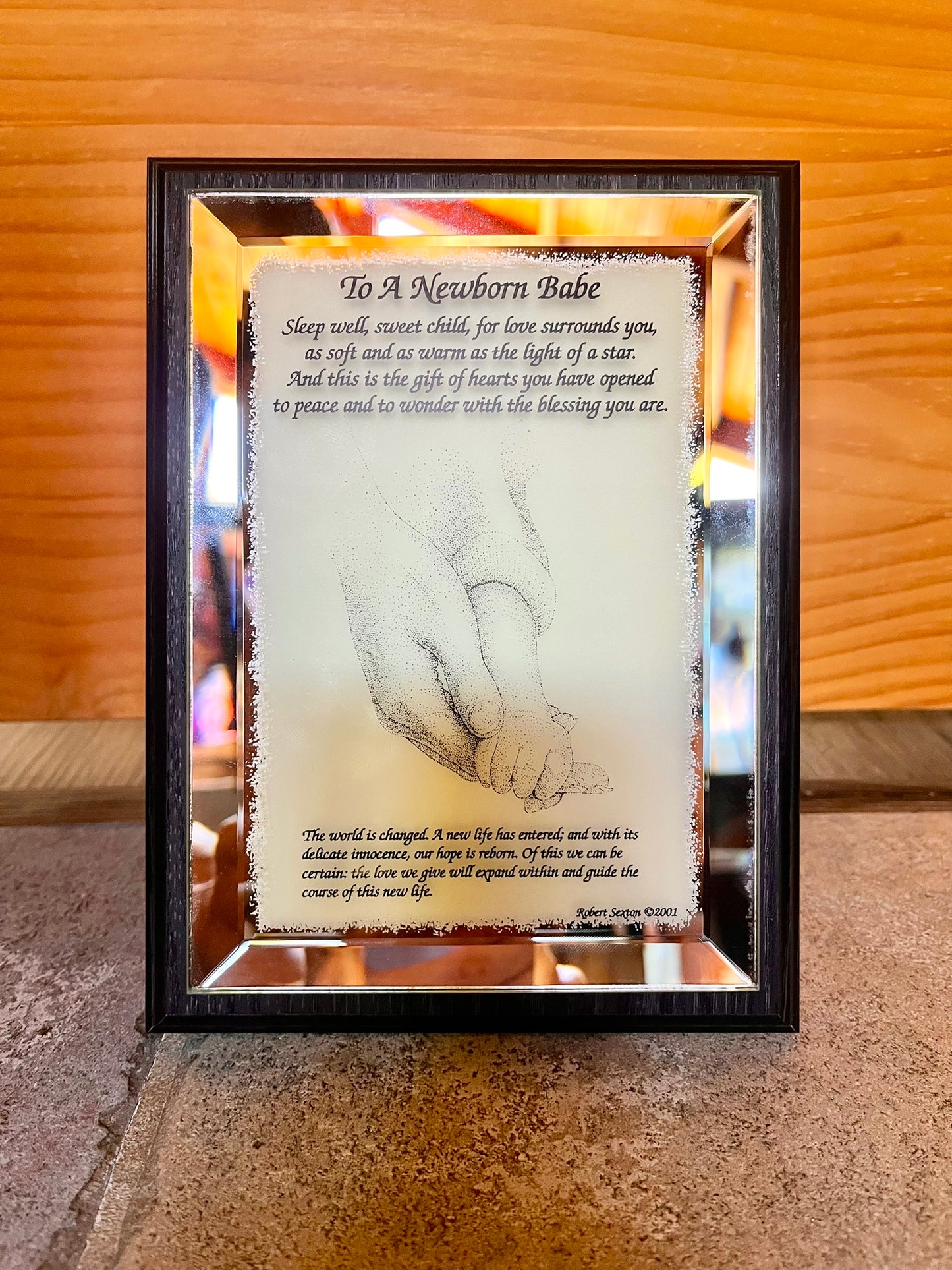 Framed artwork with a hand holding a baby's hand and a poem about a newborn babe.