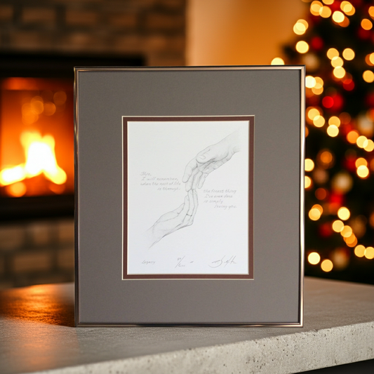 Framed artwork on a surface with a fireplace and Christmas lights in the background