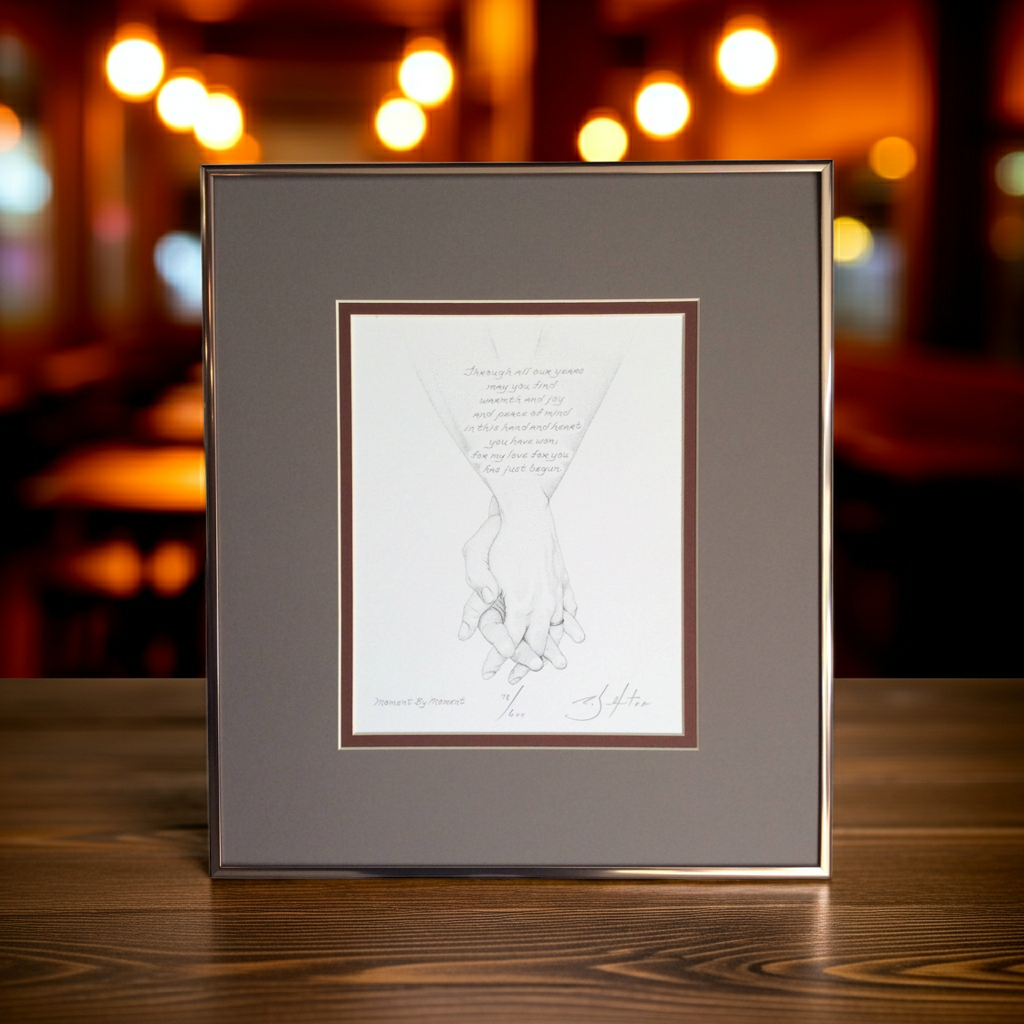 Framed artwork of holding hands  on a wooden surface with blurred lights in the background